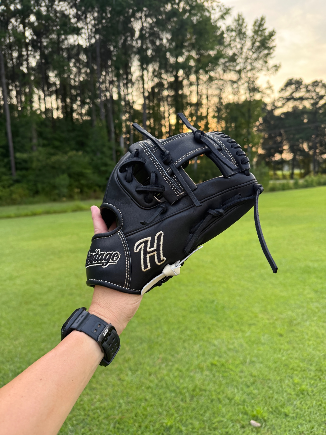 Black Heritage glove with gold 'H' embroidery held at sunset